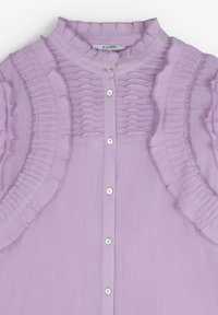 Blouse lavande avec bordure froncée le long des épaules et du devant de la poitrine, encolure ronde et boutons blancs au centre.