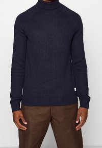 Laivastonsininen ribbineulottu pooloneule, jossa on vartalonmyötäinen leikkaus ja teksturoitu pinta, pitkät hihat ja pieni logokoriste.