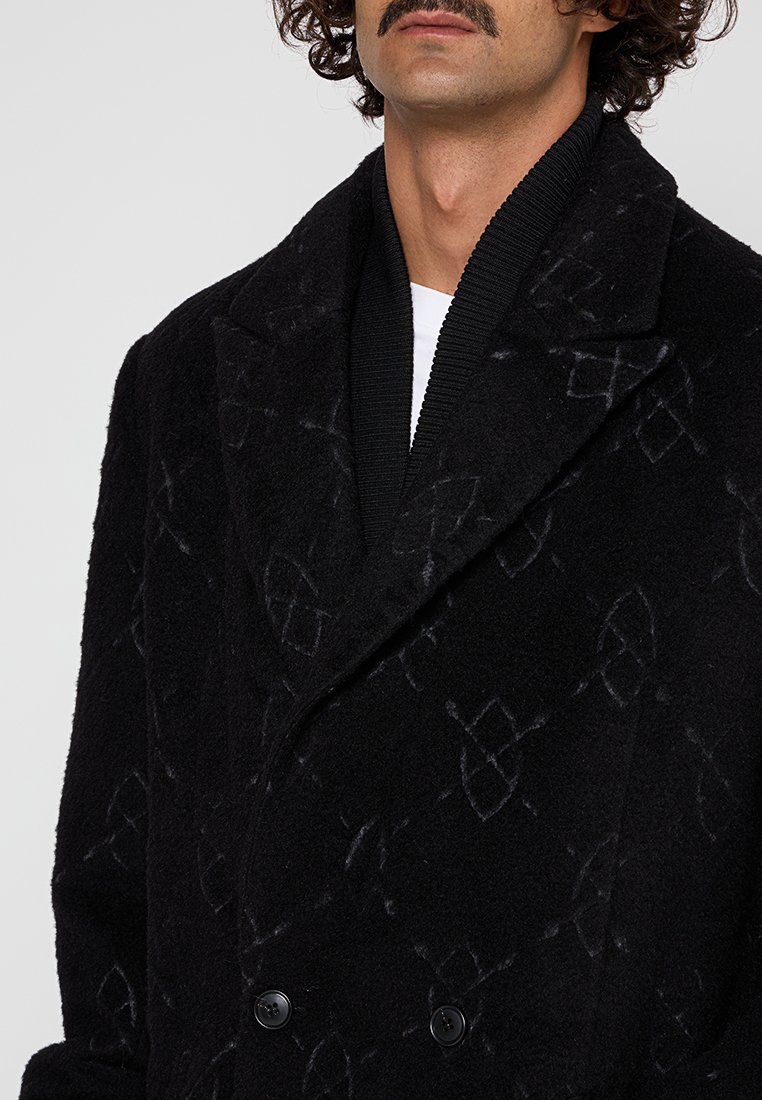 Manteau noir en mélange de laine avec une surface texturée, design à double boutonnage, boutons avant visibles et motifs géométriques subtils.