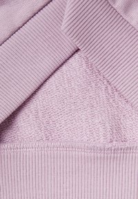 Tessuto a maglia di un leggero colore viola con varie texture: sezioni a coste e una superficie liscia e ondulata, che evidenziano motivi e cuciture contrastanti.