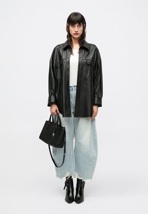 Chemise surdimensionnée en cuir noir, débardeur blanc en dessous, jeans à jambes larges bleu clair avec ourlets effilochés, bottines en cuir noir et sac à main noir.