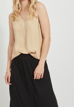 Beige, mouwloze top met V-hals, gecombineerd met een zwarte, geplooide, lange rok. De stof lijkt soepel en lichtgewicht, wat een ontspannen silhouet creëert.