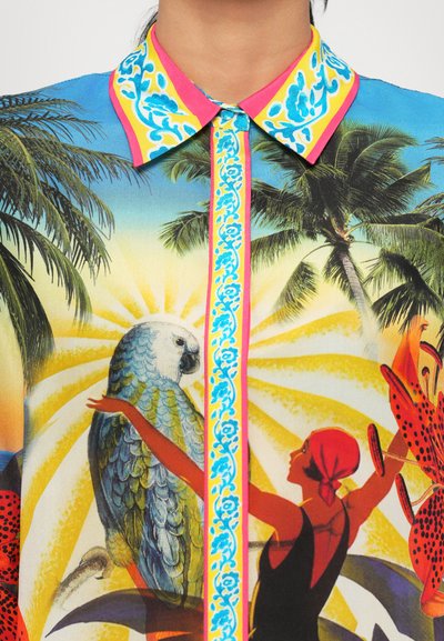 Chemise colorée à manches courtes ornée d'un imprimé tropical avec un perroquet, des palmiers et une silhouette, accentuée par un design de col vif.