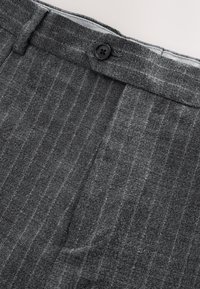 Pantalon gris à fines rayures avec une fermeture par bouton noir et des coutures visibles à la ceinture.