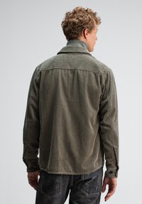 Olivgrünes Cordhemd mit vertikalen Streifen, Knopfmanschetten und klassischem Kragen. Strukturierter Stoff mit lockerer Passform und Rückenpasse.