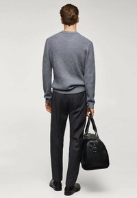 Szary sweter w wzory z ściągaczami na mankietach, zestawiony z ciemnymi spodniami. Model trzyma czarną skórzaną torbę o zaokrąglonym kształcie.