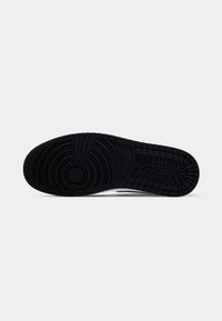 Black Nike shoe sole with grooved circular and rectangular tread patterns, displayed horizontally on a white background.