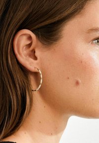 Goldener Creolen-Ohrring mit abwechselnden Perlen in Weiß und Beige, mit glatter Textur und runder Form, getragen am Ohr.