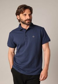 Polo en bleu marine en coton texturé, à manches courtes, avec col, patte de boutonnage à trois boutons et un petit logo sur la poitrine.
