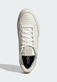 Zapatilla blanca de cuero con un acabado texturizado, que cuenta con lengua de malla, perforaciones para transpirabilidad y una suela de goma. Detalle del logo en dorado.