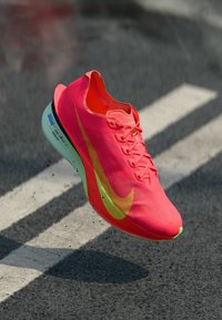 Nike-Laufschuh in leuchtendem Pink mit einer geribten Textur, gelbem Swoosh-Logo und grüner Sohle. Leichtes Design für Leistung und Geschwindigkeit.