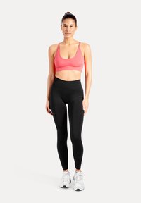 Top deportivo rosa con tirantes finos, combinado con leggings negros de talle alto. La modelo lleva zapatos deportivos blancos, con una textura de tela suave.