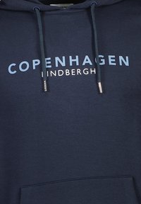 Tmavě modrá mikina s kapucí s nápisem "COPENHAGEN" a "LINDBERGH" v světle modré a bílé barvě; obsahuje nastavitelné šňůrky a přední kapsu.
