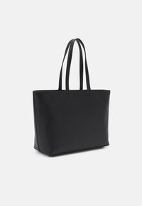 Sac fourre-tout en cuir noir avec une finition texturée, forme rectangulaire et deux longues poignées. Design minimaliste sans matériel visible.