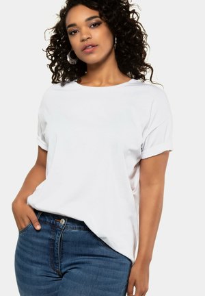 White cotton t-shirt with a relaxed fit and rolled short sleeves, paired with dark blue denim jeans. The fabric appears soft and smooth.