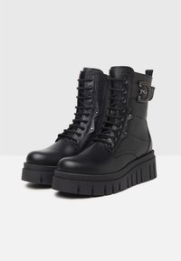 Bottines noires avec une plateforme épaisse, fabriquées avec un mélange de cuir et de textile, au design à lacets, et détail de fermeture éclair sur le côté avec des accents en métal.