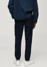 Námořnické teplákové kalhoty s elastickými manžetami, v kombinaci s denimovou košili. Mají volný střih a hladkou texturu. Bílé tenisky doplňují celý outfit.