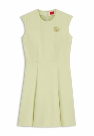 Robe sans manches vert pâle avec un col rond, une jupe plissée, une fermeture éclair au dos et une broche dorée en forme de fleur sur la poitrine.