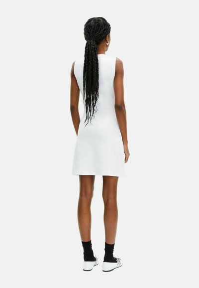 Abito bianco senza maniche con una vestibilità rilassata, che arriva a metà coscia, realizzato in tessuto liscio. Indossato con calze nere e scarpe bianche.