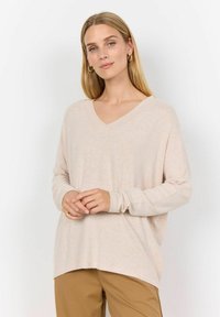 Light beige, v-neck, long-sleeve sweater in soft texture. Hemline slightly longer at back. Paired with brown pants. Simple design, no patterns.