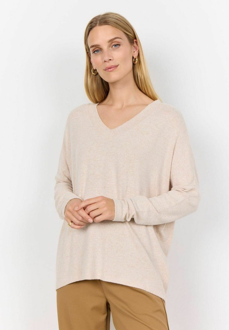 Light beige, v-neck, long-sleeve sweater in soft texture. Hemline slightly longer at back. Paired with brown pants. Simple design, no patterns.