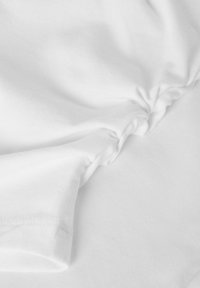 Weißer Baumwollstoff mit gerafftem Detail und glatter Textur, der die Nahtstickerei und subtile Falten zeigt.