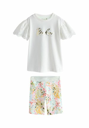 Weißes Kurzarmoberteil mit Spitzensäumen und goldenem Schriftzug "Baker by Ted Baker" kombiniert mit pastellfarbenen, floralen Shorts.