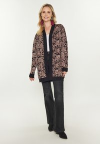 Černý cardigan s paisley vzorem v odstínech růžové, s žebrovanými manžetami a spodním lemem. Kombinovaný s černými rozšířenými džíny a špičatými botami.