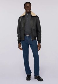 Svart skinnbombarjacka med beige konstpälskrage, dragkedjestängning, två framfickor, kombinerad med mörkblå jeans och svarta skor.