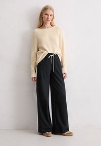 Beige geribbelde gebreide trui met een brede halslijn, gecombineerd met losse zwarte broek met een elastische tailleband en witte zijstroken.