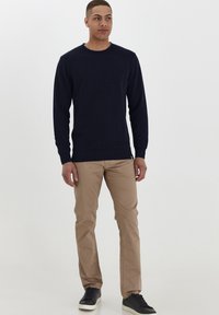 Marineblauwe lange mouwen trui met ronde hals, beige slim-fit broek en zwarte sneakers. Zachte textuur met geribde manchetten en zoom. Casual outfit.