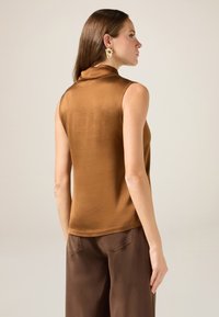 Bruine mouwloze top met een hoge kraag, gemaakt van gladde, licht glanzende stof. Te combineren met donkerbruine losse broek.