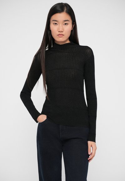 Bluză neagră cu mâneci lungi, din tricot ribbed, cu guler fals și tiv ondulat, purtată cu pantaloni din denim închis. Prezintă o siluetă ajustată.