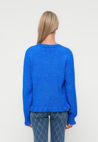 Pull en maille bleu avec un col rond et des manches longues. Texture douce, ourlet côtelé et coupe décontractée. Assorti à un jean à carreaux.