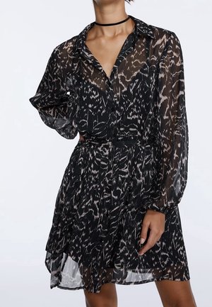 Vrouw draagt een doorschijnende zwart-witte jurk met lange mouwen, een patroon, een kraag en een choker ketting.