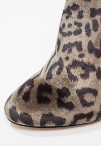 Primer plano de una bota de tobillo con estampado de leopardo en un tejido suave y texturizado, con punta redondeada sobre un fondo blanco.