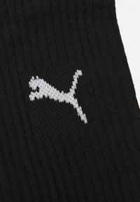 Chaussette noire en tricot arborant un logo Puma blanc. Le design comprend un motif texturé avec des détails côtelés pour plus de flexibilité.
