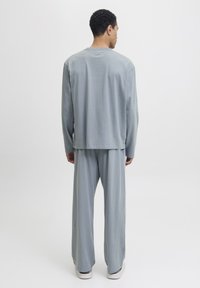 Man wearing light blue loose-fit long-sleeve top and matching wide-leg pants, standing facing away on a plain white background.