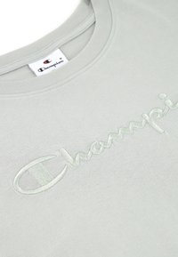 T-shirt en coton gris clair avec un logo "Champion" brodé dans une teinte pastel assortie, doté d'un col rond et d'une texture douce.