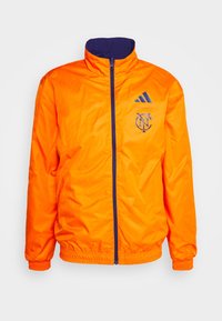 Veste zippée orange avec col montant, accents marine et détails de logo. Fabriquée en matériau lisse et léger avec des poignets élastiques.