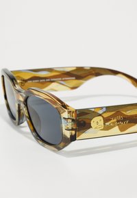 Gafas de sol de carey marrón con lentes grandes y redondeados. La montura de acetato presenta un patrón en el interior de las patillas y un detalle de diseño gráfico en el costado.