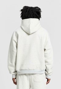 Jasnoszara bluza z kapturem o luźnym kroju, z prążkowanymi mankietami i dołem, miękką teksturą oraz średniej wielkości kapturem.