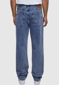 Voľné modré denim džínsy s vyšívaným logom na zadnej strane, s dvoma zadnými vreckami a manžetami na spodnej časti. Hladká textúra.