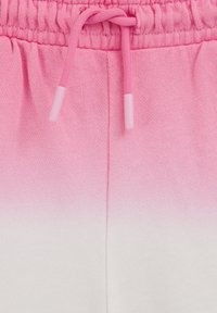 Gros plan sur un tissu ombré rose à blanc avec une ceinture élastique et un cordon de serrage noué sur un pantalon de survêtement ou un short.