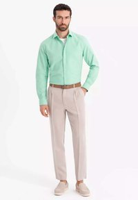 Camicia a maniche lunghe verde chiaro abbinata a pantaloni beigi a pieghe e scarpe slip-on beige, con una cintura marrone. Tessuto dalla superficie liscia.