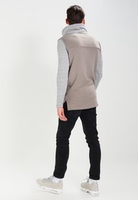 Pullover grigio con collo alto, caratterizzato da maniche grigie chiare. Indossato con pantaloni neri e sneakers grigie. Tessuto morbido con una vestibilità rilassata.