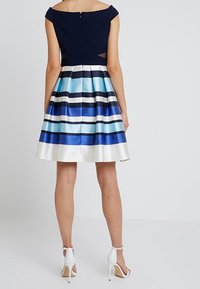 Šaty s kapkovými rukávy, které mají námořnický korzet a rozšířenou sukni s vodorovnými modro-bílými pruhy. Obsahují zip na zadní straně a strukturovanou tkaninu.