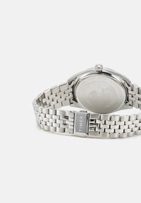 Montre en acier inoxydable argenté avec un bracelet en maille et un boîtier rond. Dotée d'un cadran texturé et d'un fermoir avec gravure "TIMEX". Résistante à l'eau jusqu'à 50 mètres.
