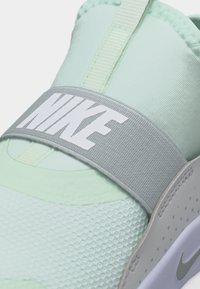 Ανοιχτό πράσινο αθλητικό παπούτσι Nike με υφή στη μύτη, γκρι ελαστικό λουράκι στο πάνω μέρος με λευκό κείμενο "NIKE" και γκρι λεπτομέρεια στο πλάι.