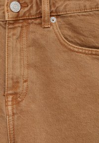 Jeans en denim de coton de couleur marron clair avec une texture délavée. Comprend un bouton en métal, des coutures contrastées et une poche avant.